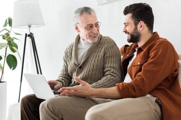 Happy Bearded Man Gesturing While Sitting Senior Father Looking Laptop — Stock Photo, Image