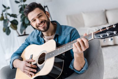 neşeli sakallı adam evde akustik gitar çalmak