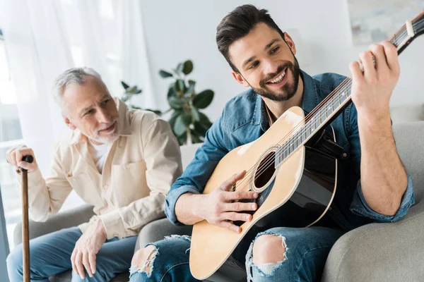 Alegre Barbudo Hombre Tocando Guitarra Acústica Cerca Padre Mayor Casa — Foto de Stock