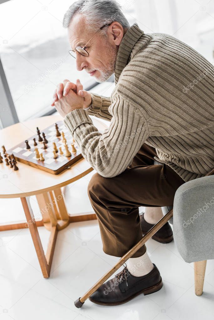 overhead view of senior man thinking while sitting near chess board at home