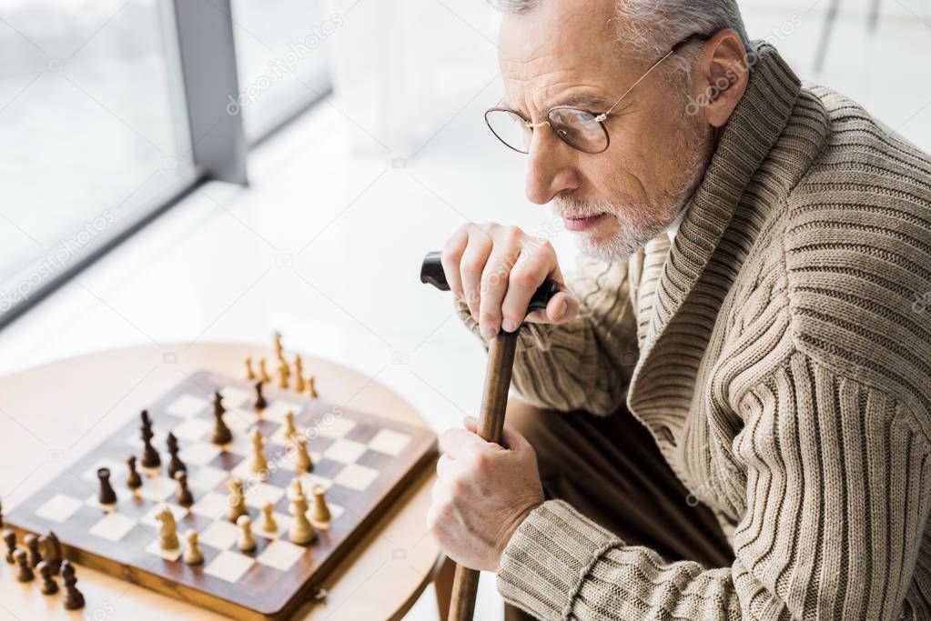 overhead view of retired man in glasses thinking while sitting near chess board at home