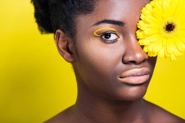 Sarı üzerinde kamera bakarak çiçek ile çarpıcı Afrikalı Amerikalı kadın 