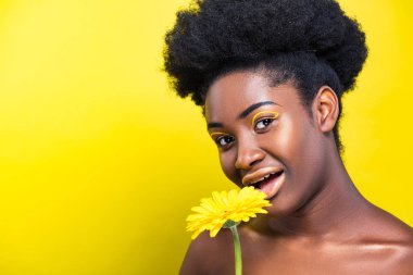 Sarı üzerinde kamera bakarak çiçek ile çarpıcı Afrikalı Amerikalı kadın 