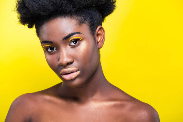 Attractive african american woman with trendy makeup looking at camera isolated on yellow