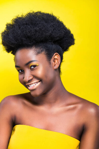 Joyful smiling african american girl with makeup isolated on yellow