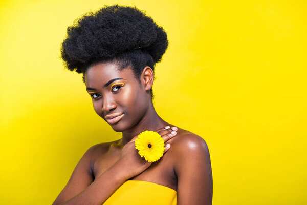 Pretty african american girl with flower looking at camera on yellow