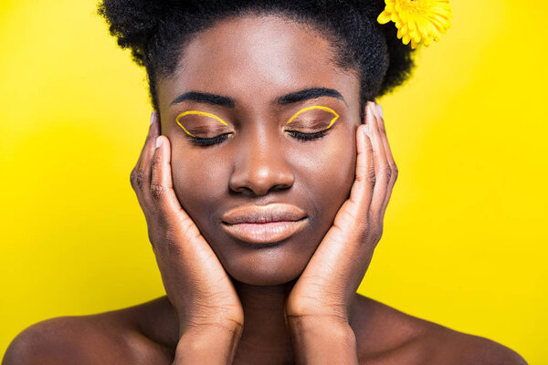 African american girl with closed eyes with flower in hair isolated on yellow