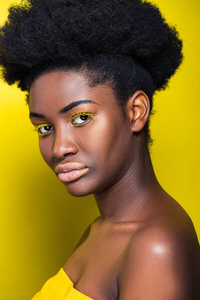Beautiful african american woman with bright eyelashes looking at camera on yellow
