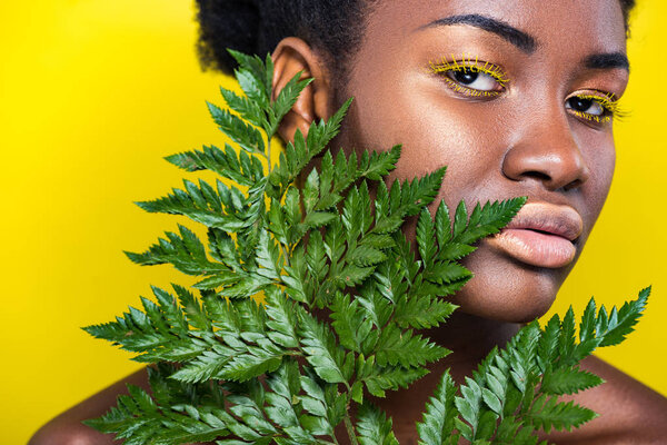 Beautiful african american girl with green fern isolated on yellow