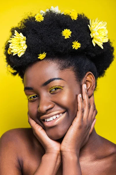 Smiling african american girl with flowers in hair looking at camera isolated on yellow