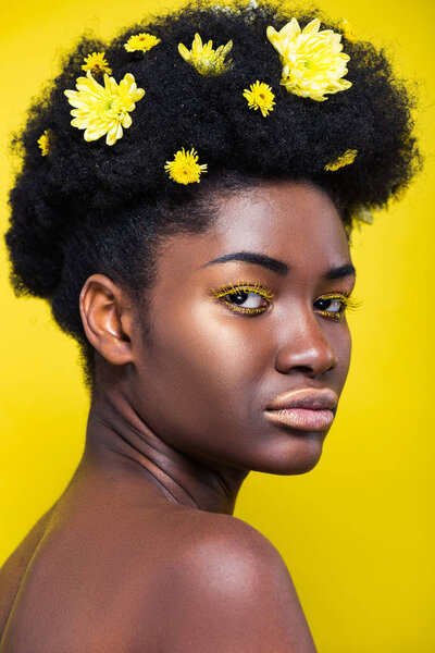 Beautiful african american woman with chrysanthemums in hair isolated on yellow