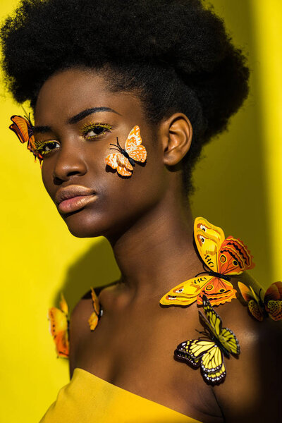 Attractive african american young woman with butterflies on yellow