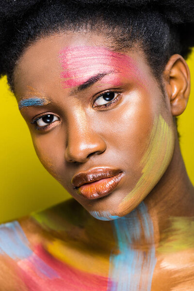 Serious african american woman with body art looking at camera on yellow