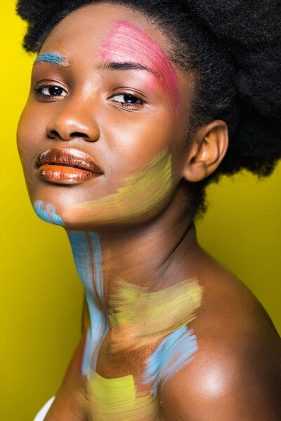 Attractive african american woman with bright makeup looking at camera on yellow