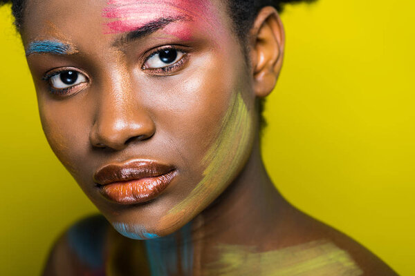 Attractive african american woman with bright makeup looking at camera on yellow