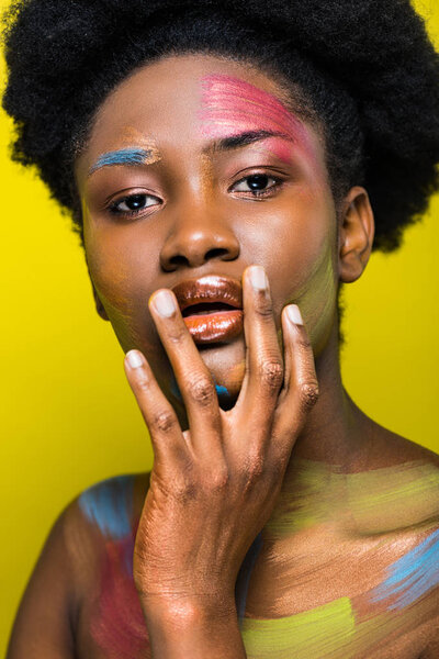 Interested african american woman with body art touching lips and looking at camera