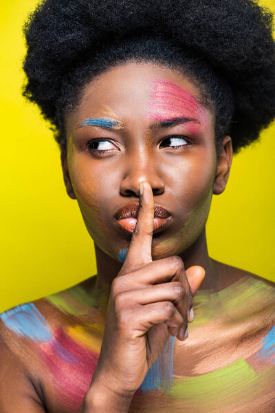 Африканская американка с ярким макияжем демонстрирует молчаливый жест, изолированный на желтом
