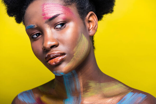 Pensive african american woman with colorful body art on yellow