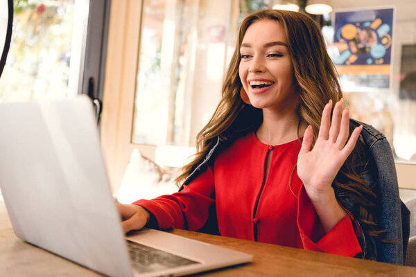 веселый блоггер машет рукой во время видеозвонка на ноутбуке
 