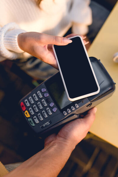 top view of young woman paying with smartphone in cafe 