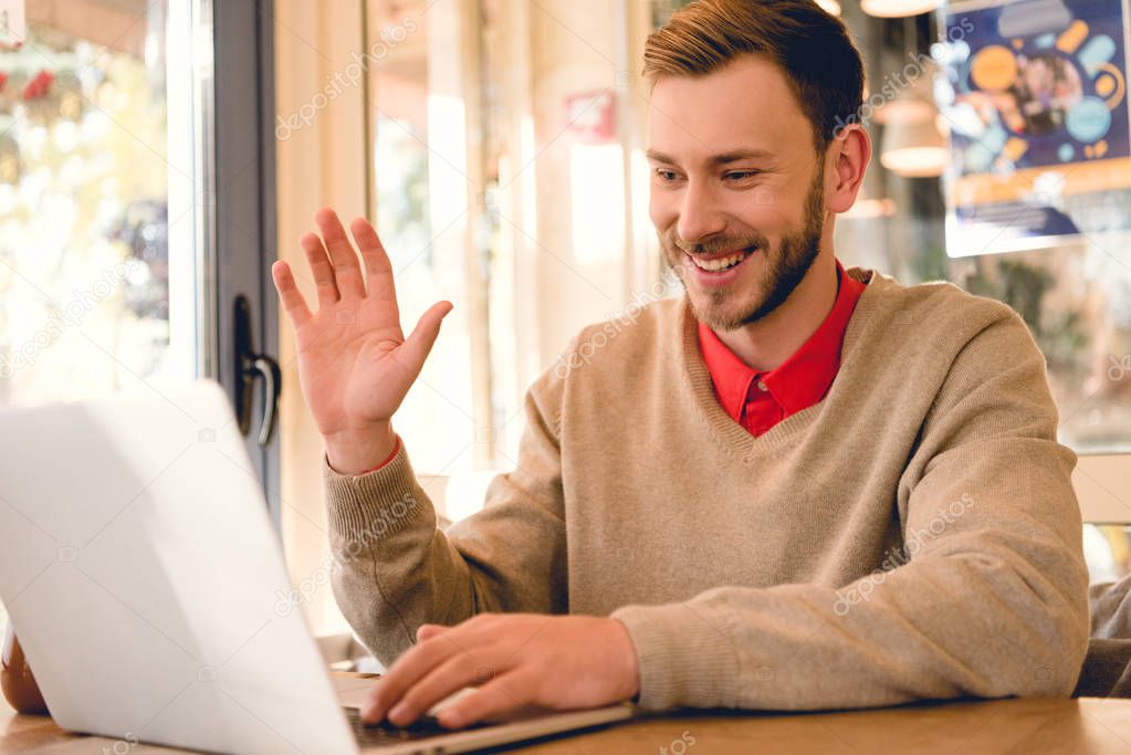 cheerful freelancer waving hand while having video call on laptop 