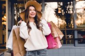 happy young woman in hat smiling while holding shopping bags 