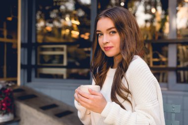 attractive young woman holding cup with coffee in cafe  clipart