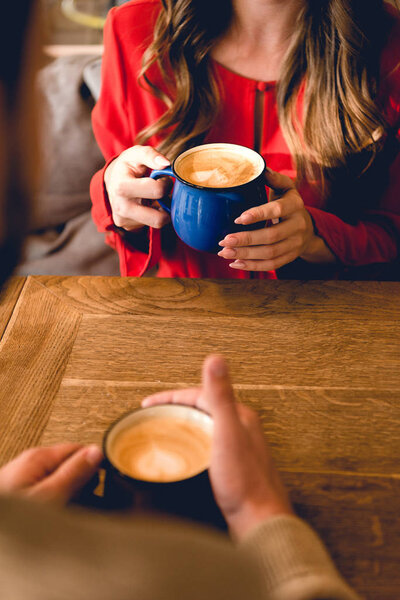 cropped view of man and woman holding cups with coffee in cafe 