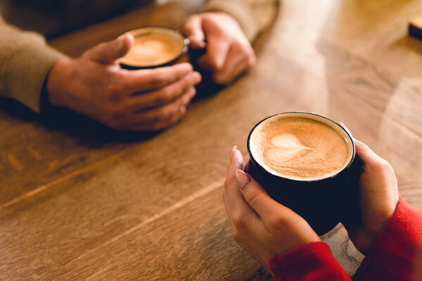 cropped view of man and young woman holding cups with coffee in cafe 