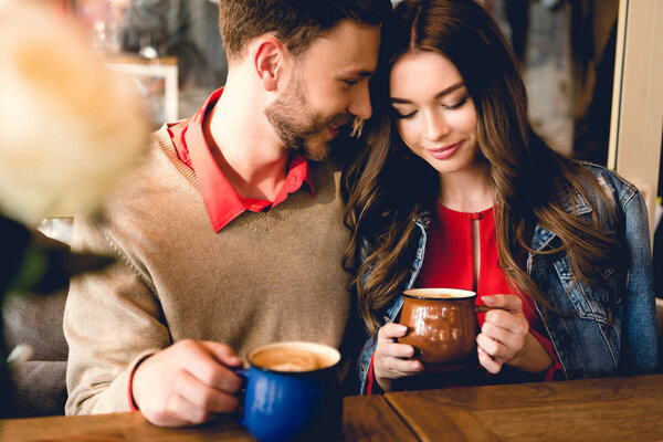 happy bearded man looking at attractive girlfriend while holding cup of coffee