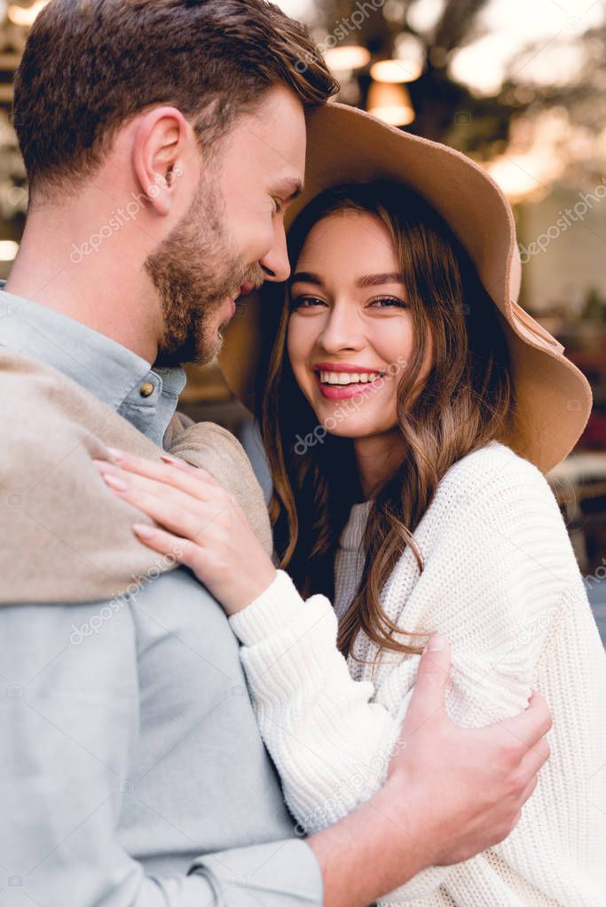 cheerful young woman in hat hugging happy boyfriend 