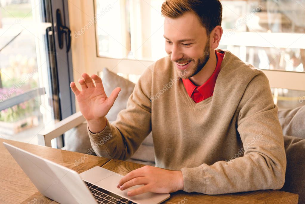 cheerful blogger waving hand while having video chat on laptop 