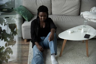 Bir kadın yerde oturur, oturma odasında bunalmış ve üzgün hisseder, düşünceleriyle baş başa..