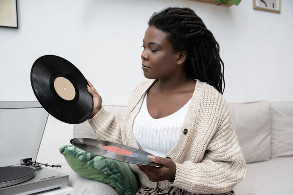 A woman with braided hair listens to vinyl records while relaxing in her modern apartment.