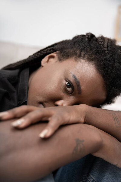 A woman with braided hair sits at home, feeling overwhelmed by sadness and emotions.