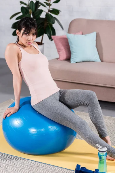 Ajuste jovem mulher relaxante na bola em forma e olhando para a câmera em casa — Fotografia de Stock