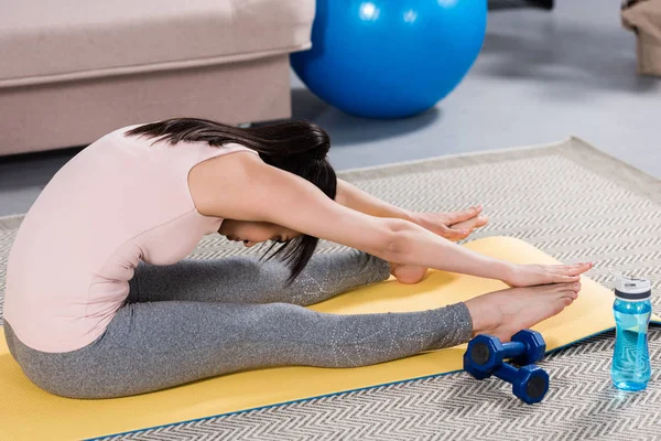 Hermosa joven haciendo adelante curva en yoga mat en casa - foto de stock