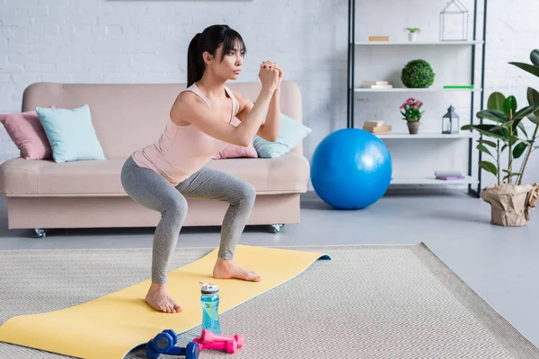 Підходить молода жінка робить присідання на йога килимок вдома — стокове фото