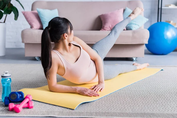 Bella giovane donna sdraiata su tappetino yoga e sollevamento gamba a casa — Foto stock