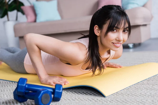 Souriant jeune femme travaillant sur tapis de yoga à la maison et regardant la caméra — Photo de stock