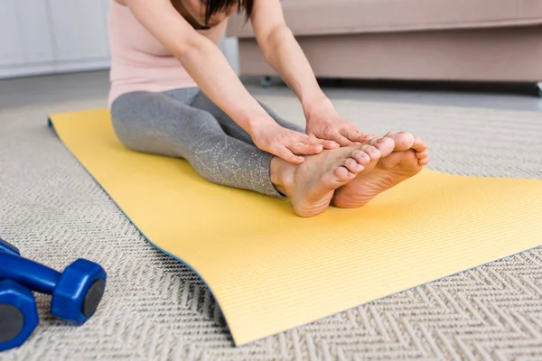 Cropped shot of woman doing forward bend on yoga mat at home — Stock Photo