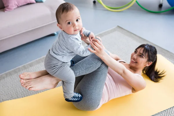 Blick aus der Vogelperspektive auf junge schöne Mutter, die mit ihrem kleinen Kind zu Hause auf der Yogamatte trainiert — Stockfoto