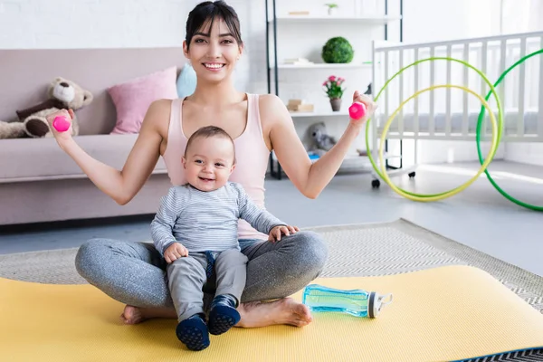 Joven madre deportiva con un niño feliz sentado en la esterilla de yoga y haciendo ejercicios en casa — Stock Photo