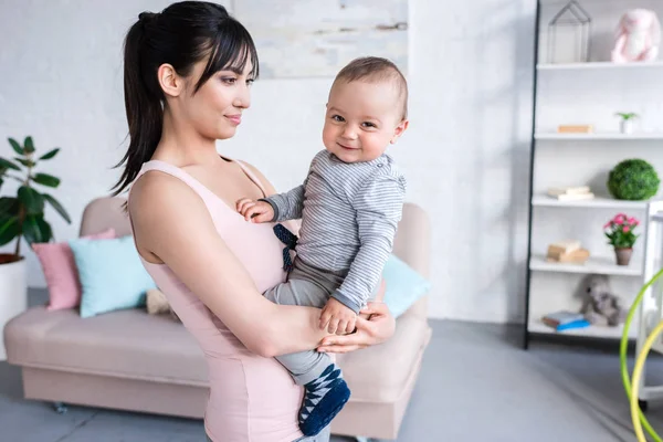 Hermosa joven madre sosteniendo a su pequeño hijo en casa - foto de stock