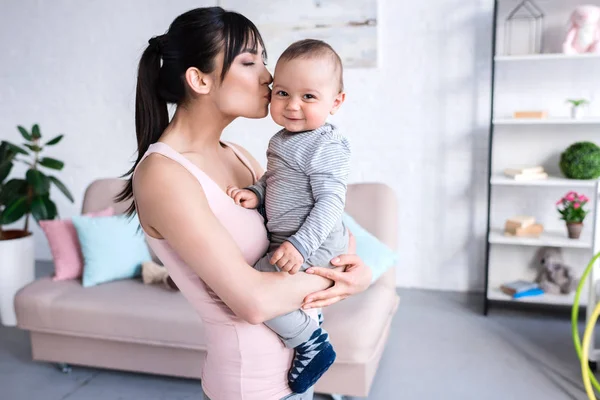 Schöne junge Mutter küsst ihr kleines Kind zu Hause — Stockfoto