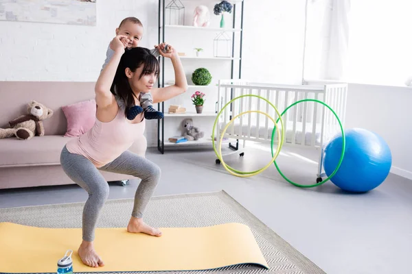 Young sportive mother carrying her little child on shoulders while doing squats — Stock Photo