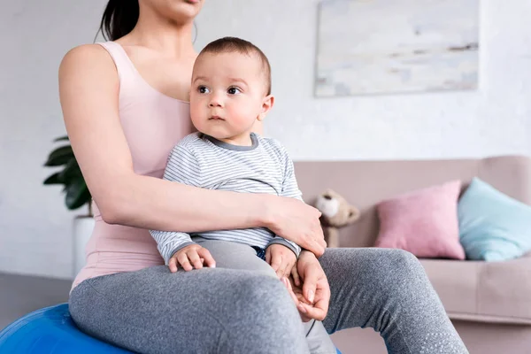 Cropped shot of mother sitting on fit ball with little child at home — Stock Photo