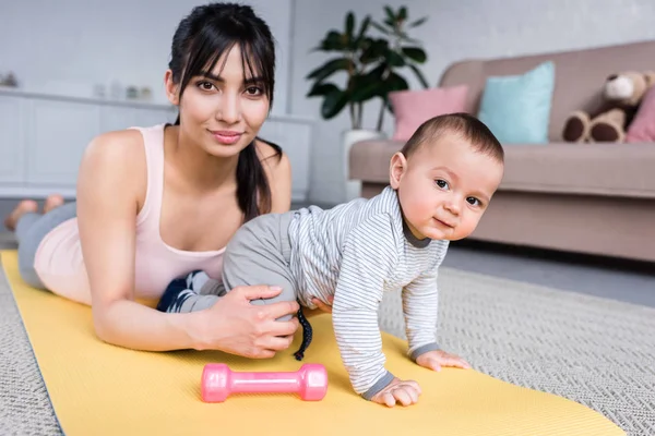 Junge glückliche Mutter und kleines Kind zu Hause auf Yogamatte und schauen in die Kamera — Stockfoto