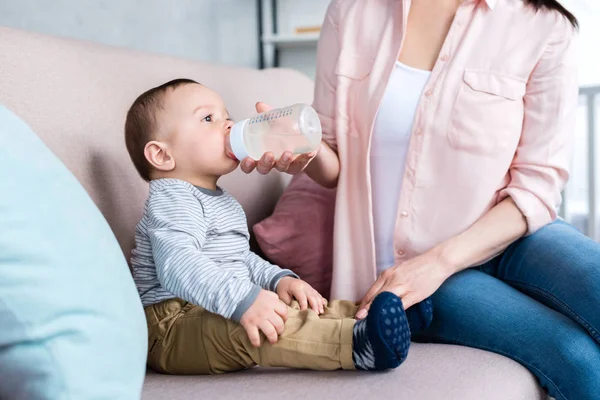 Schnappschuss von Mutter, die ihr kleines Kind zu Hause mit Flasche füttert — Stockfoto