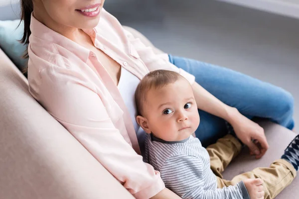 Cropped shot of young mother and little child sitting together on couch at home — Stock Photo